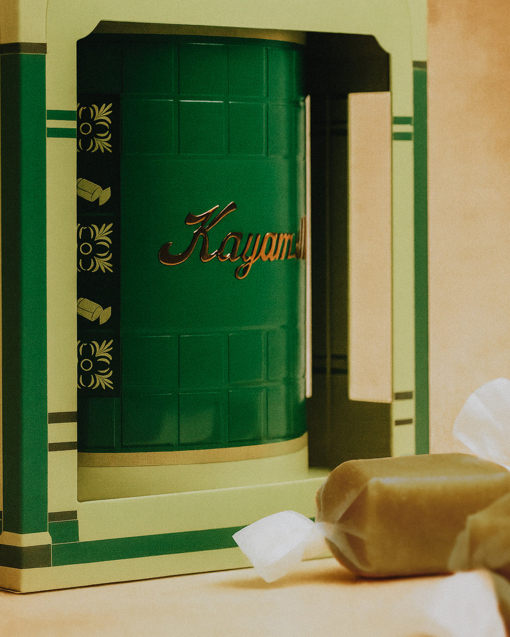 Green cylindrical container with 'Kayamel' branding on a decorative box with candies surrounding it.